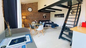 A modern living space with a brick wall, a dining area with a glass table, a sofa, and a staircase.