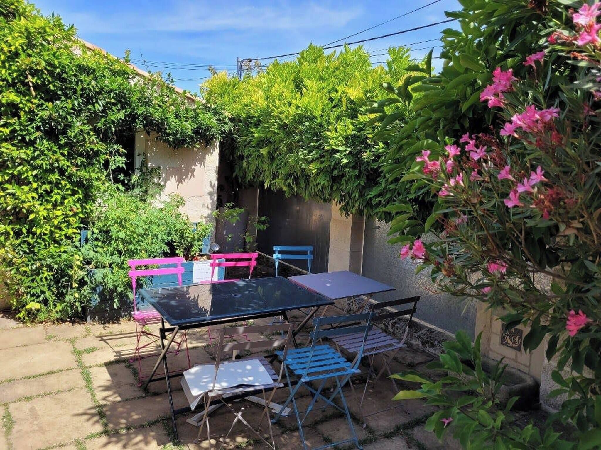An outdoor patio with a table and chairs, surrounded by lush greenery and flowering plants.