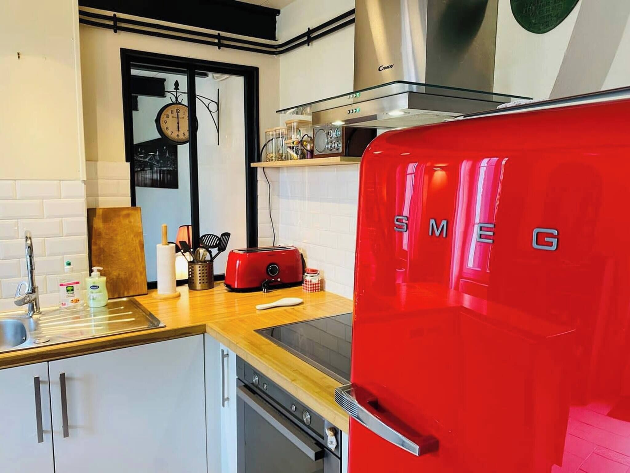 A kitchen with a red SMEG refrigerator, a wooden countertop, a sink, and a clock on the wall.