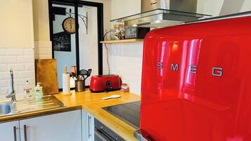 A kitchen with a red SMEG refrigerator, a wooden countertop, a sink, and a clock on the wall.