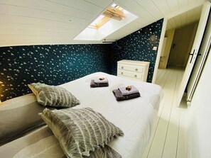 A bedroom with a skylight, a bed with pillows, a nightstand, and a dresser.