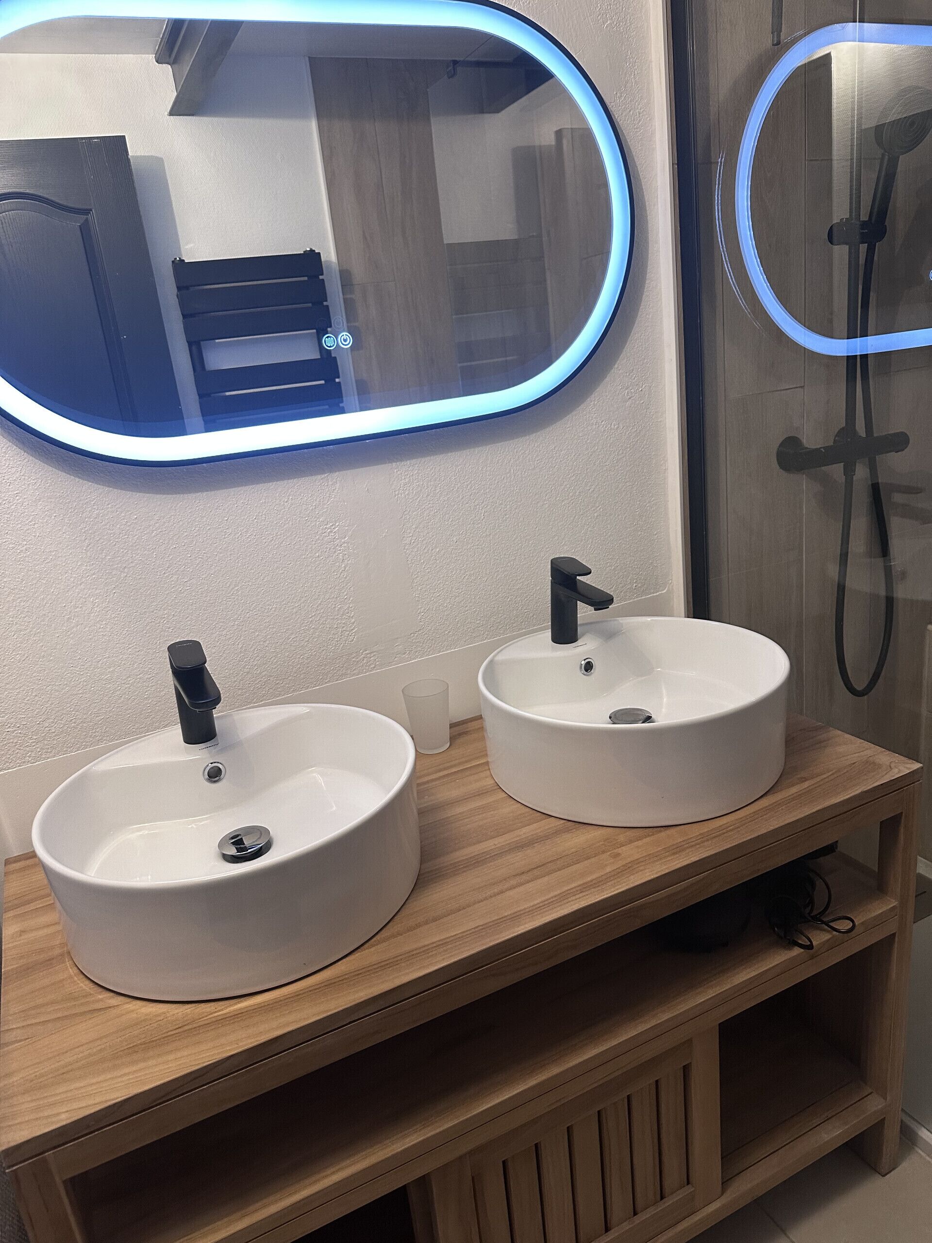 A bathroom with two white sinks, a mirror with a blue light, and a shower area.