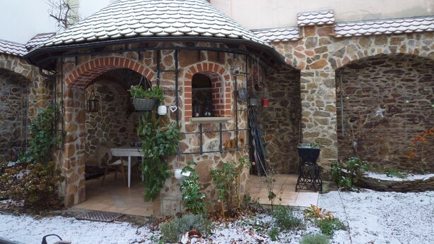 A stone building with a tiled roof, a small patio area, and a brick fireplace.