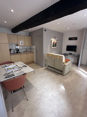 A modern kitchen with wooden cabinets, a dining table with chairs, a sofa, and a TV.