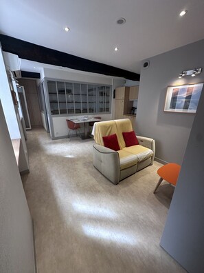 A modern living room with a sofa, a dining table, and a kitchen area in the background.