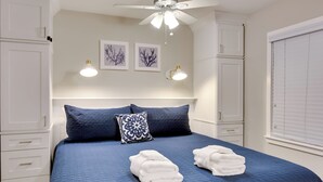 Una cama bien hecha con un edredón azul, dos toallas blancas y una almohada decorativa.