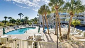 A poolside area with lounge chairs, palm trees, and a multi-story building in the background. - Oceanfront Breakers 137 Condo w/ Sunrise Views! (Hilton Head Island)