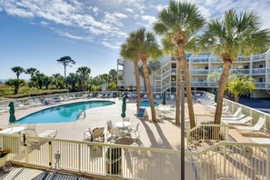 A poolside area with lounge chairs, palm trees, and a multi-story building in the background. - Oceanfront Breakers 137 Condo w/ Sunrise Views! (Hilton Head Island)