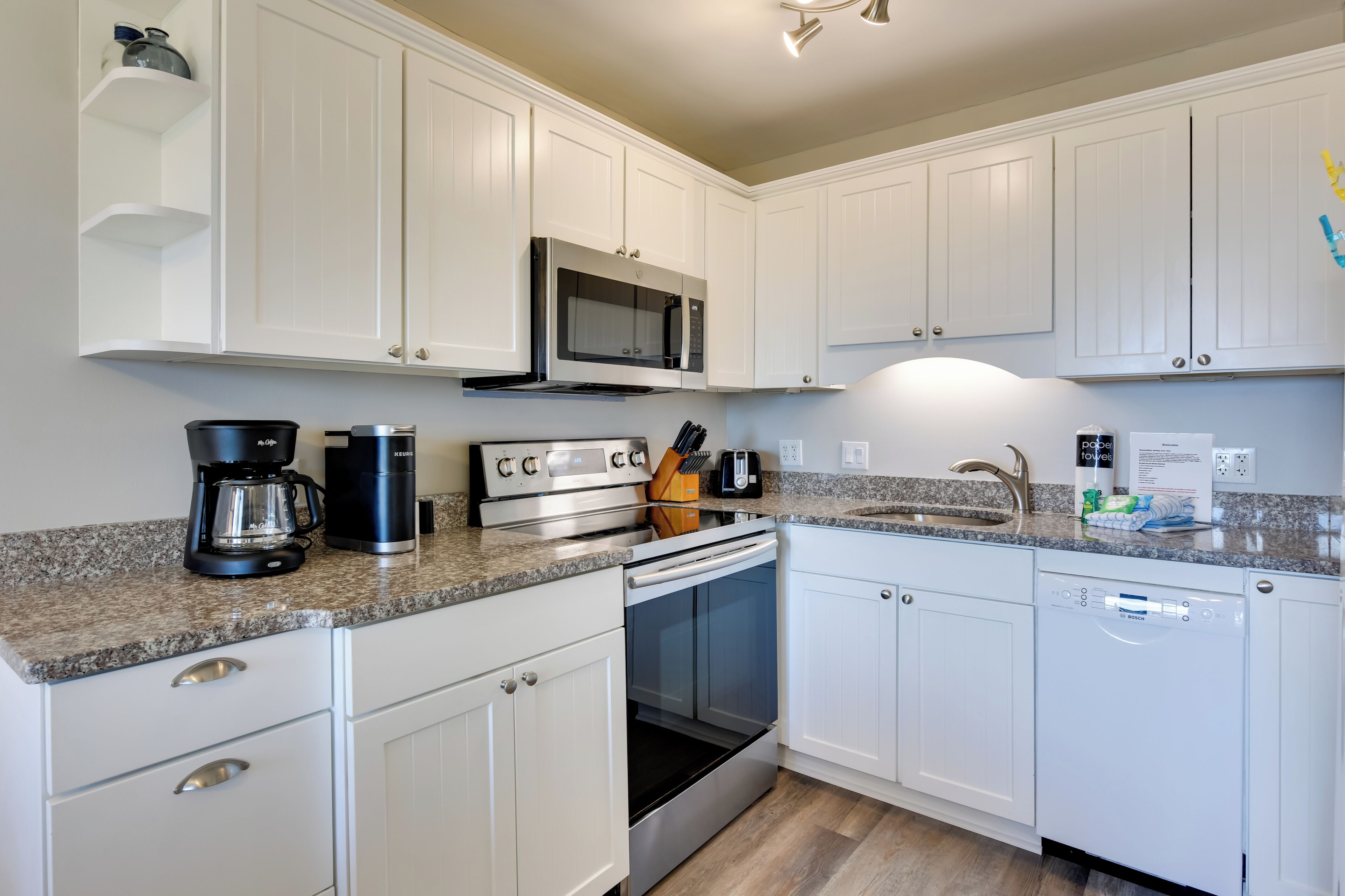 A modern kitchen with white cabinets, a stainless steel microwave, a coffee maker, and a dishwasher.