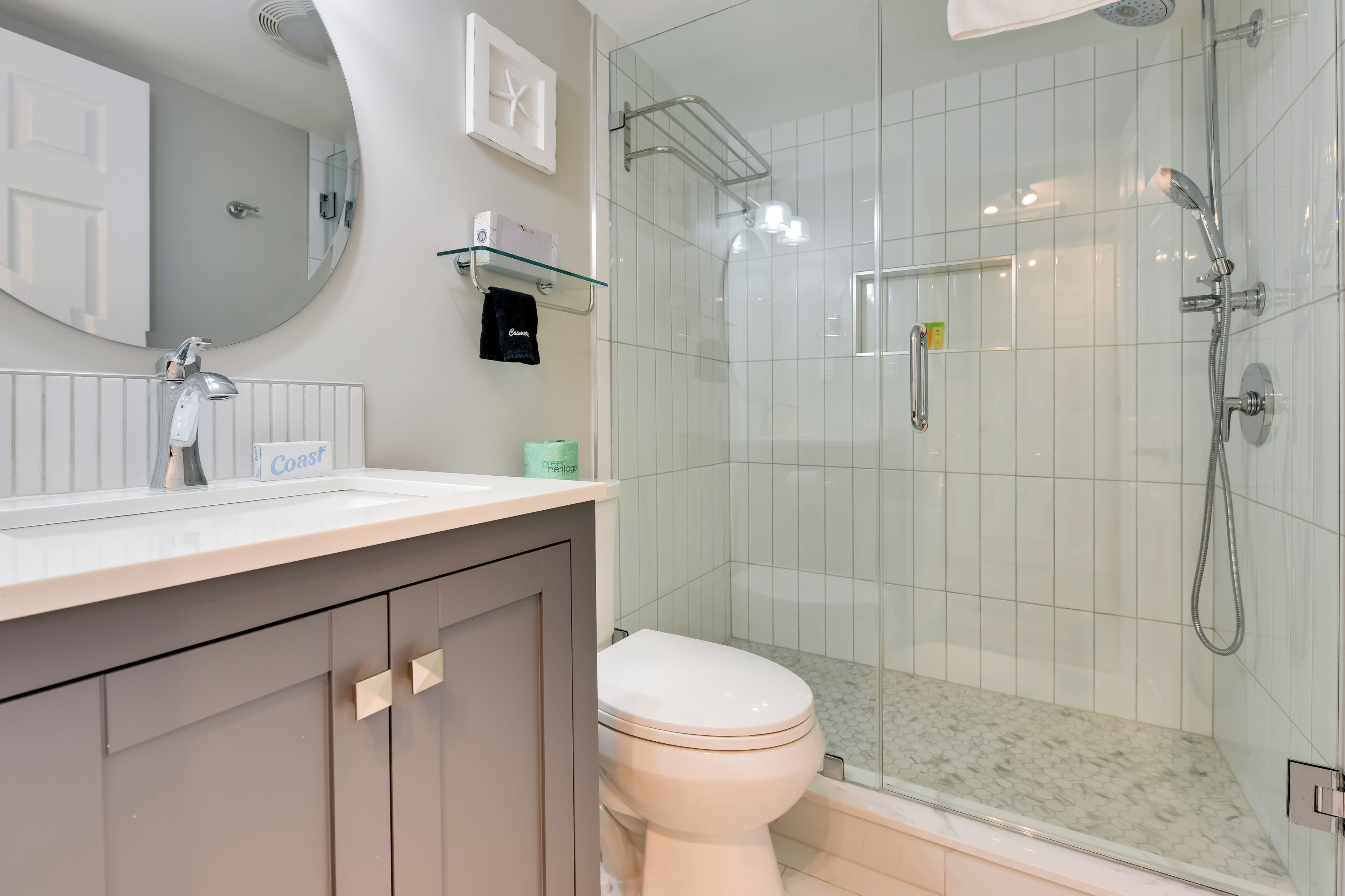 Ein modernes Badezimmer mit Toilette in Weiß, einer gläsernen Dusche und einem Waschtisch mit Spiegel und Seifenspender.