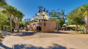 A pirate-themed play area with a ship structure, palm trees, and a sandy ground. - Oceanfront Condo! Breakers 210 w/ Sunrise Views (Hilton Head Island)