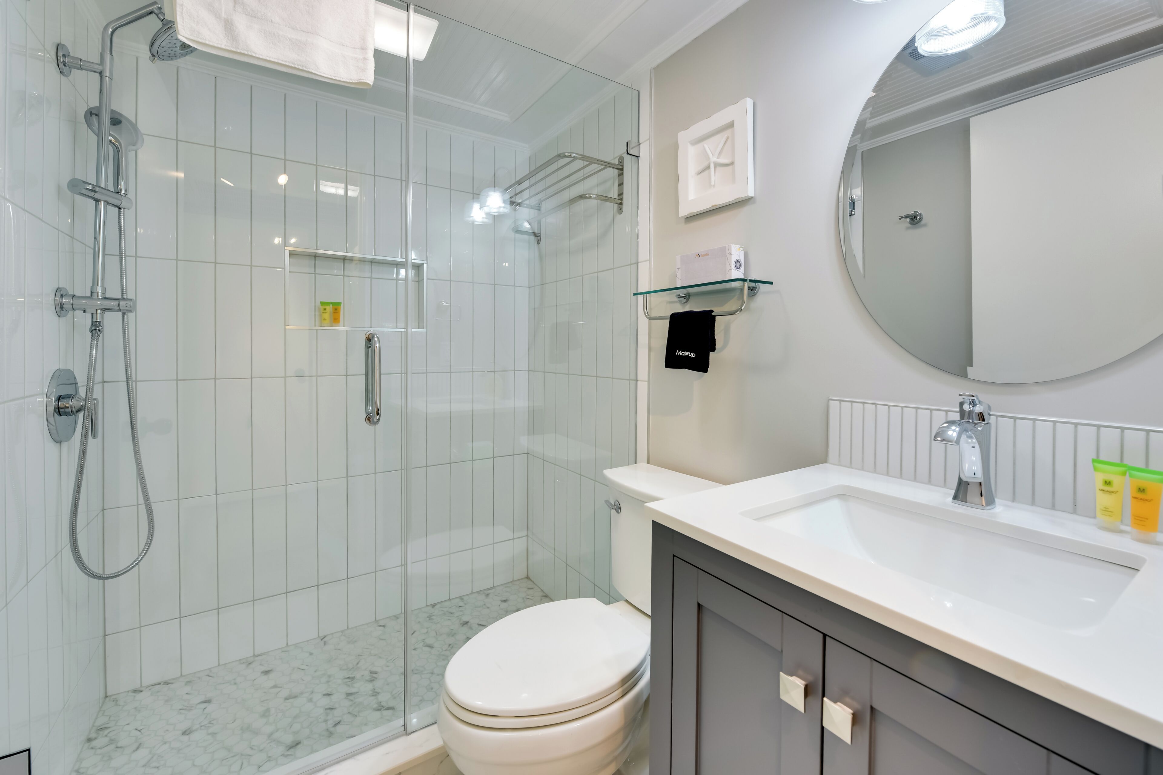A modern bathroom with a glass-enclosed shower, a white toilet, a large mirror, and a sink with toiletries.