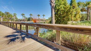 A wooden boardwalk with a metal railing, surrounded by palm trees and other vegetation. - Oceanfront Condo! Breakers 210 w/ Sunrise Views (Hilton Head Island)