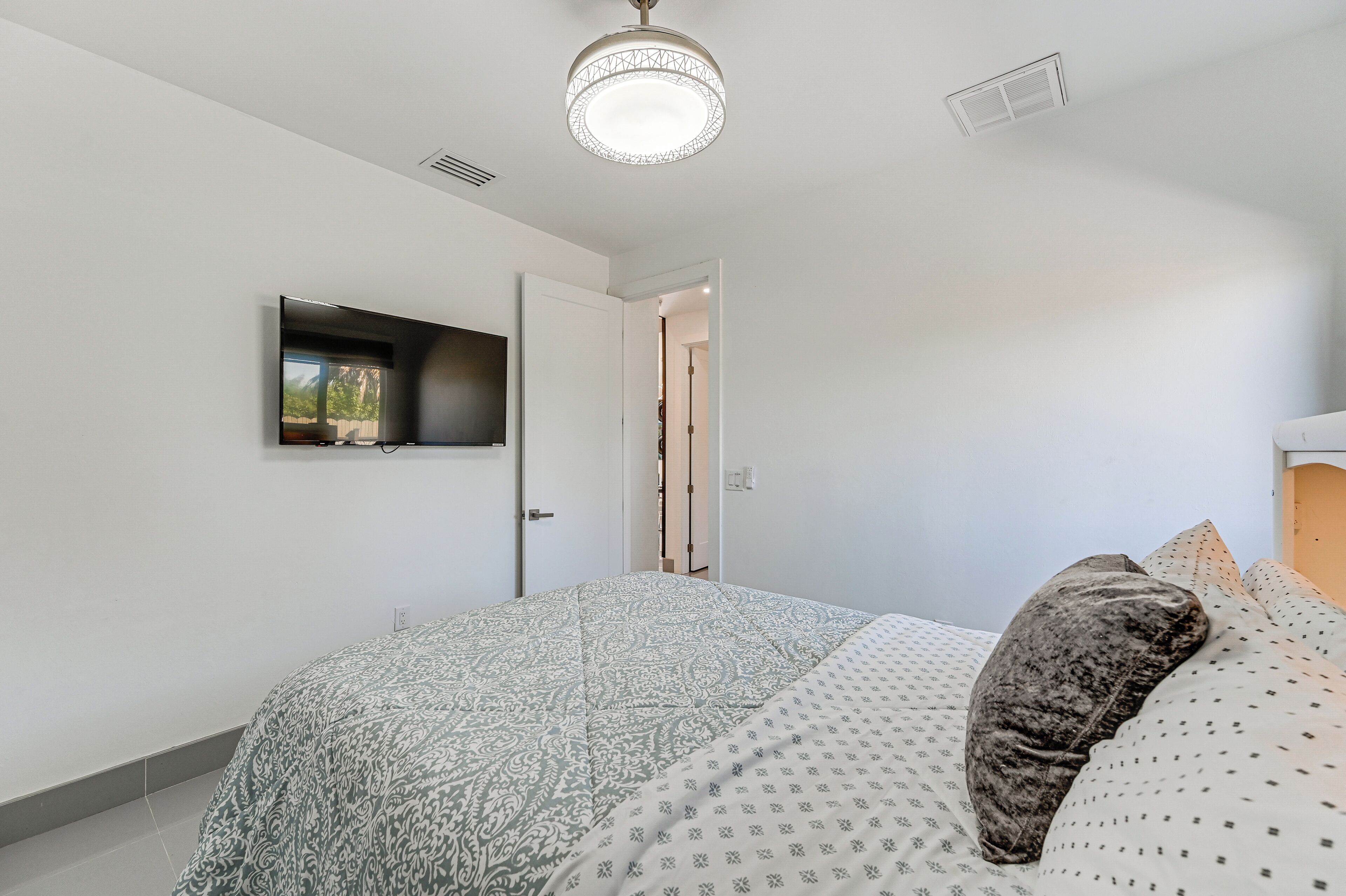 Een slaapkamer met een bed, een flatscreen-televisie aan de muur en een plafondlamp.