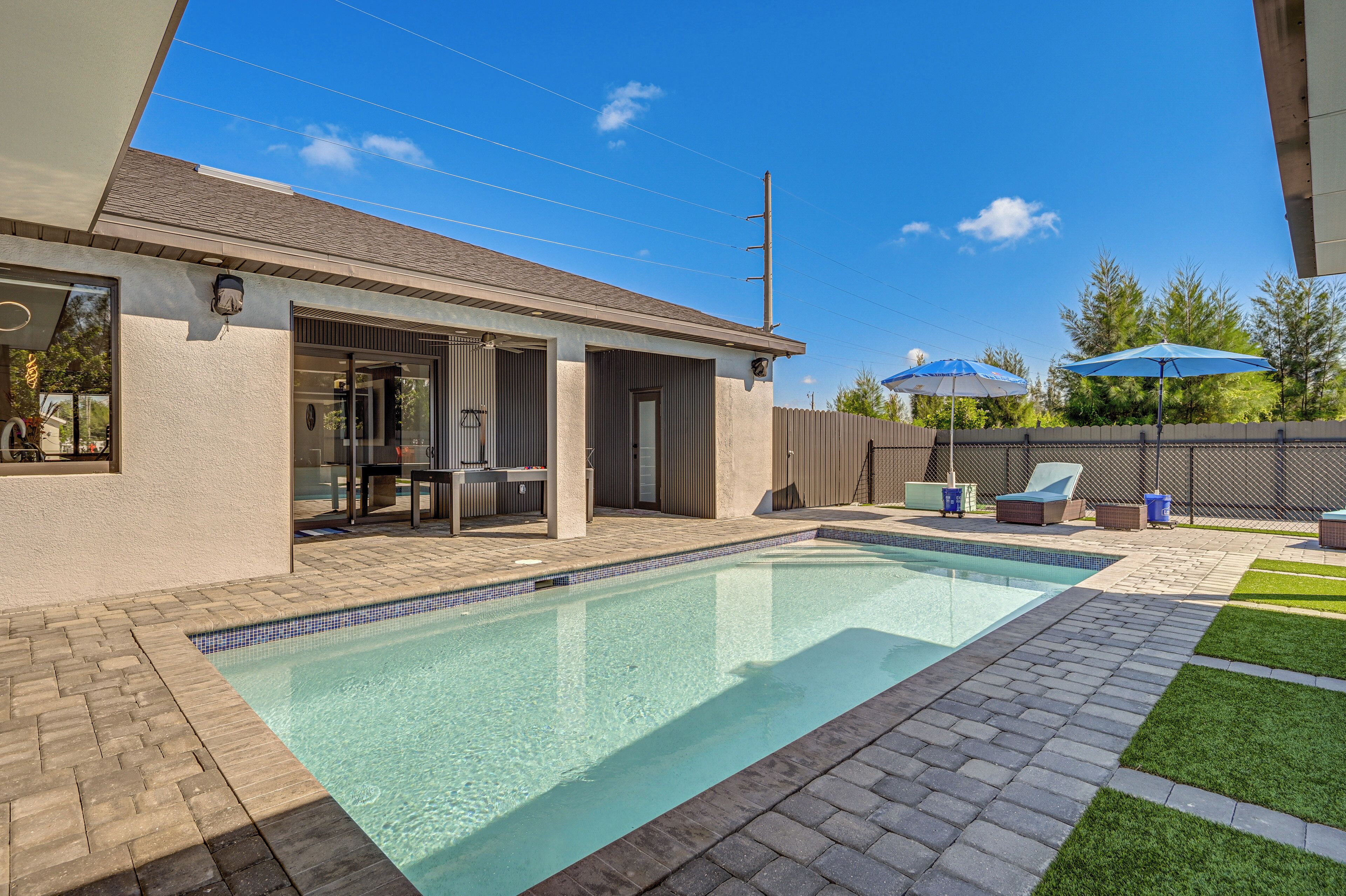Piscina com borda azulejada, área de terraço com mobiliário ao ar livre e espaço de estar coberto.