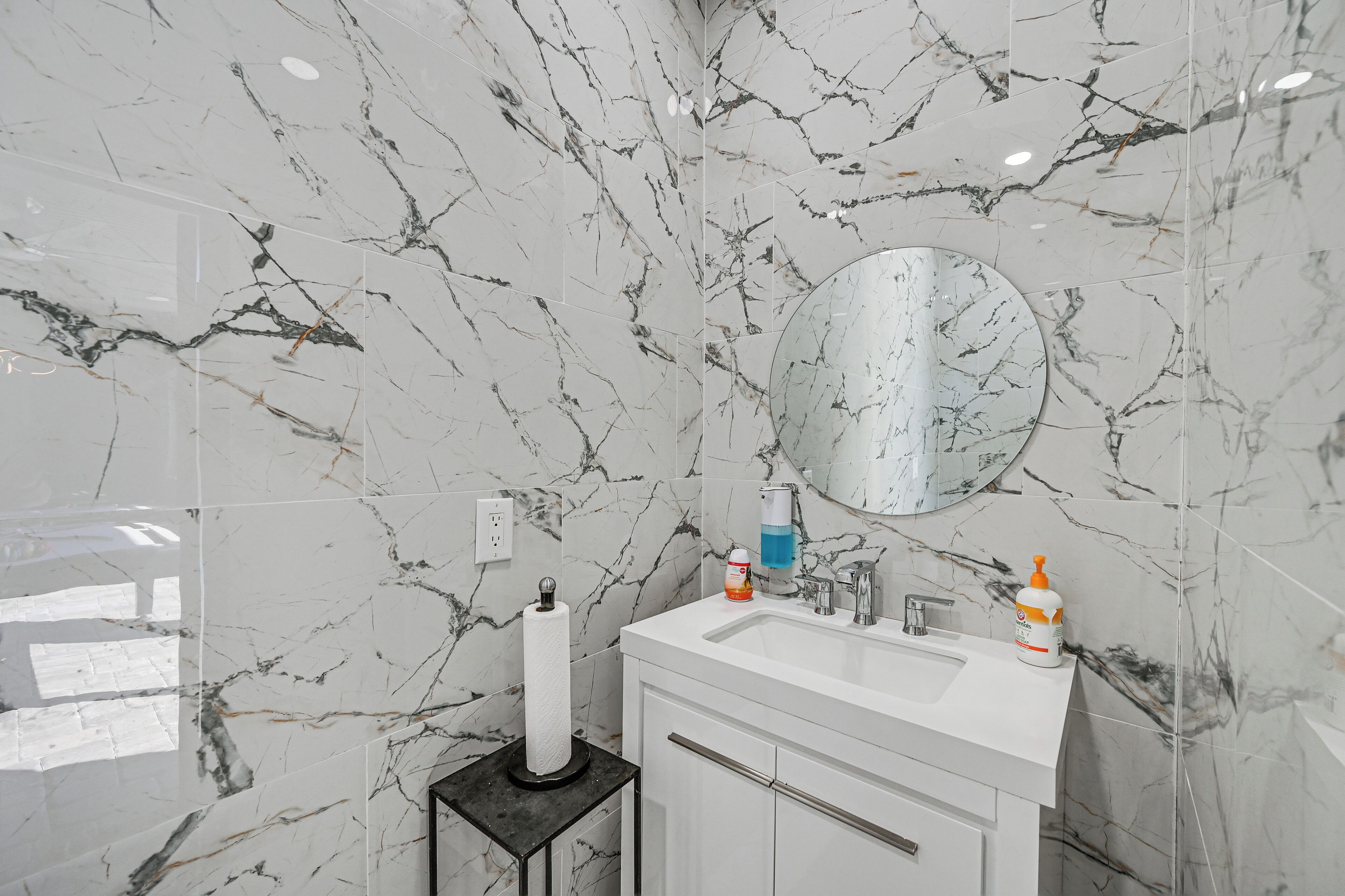 A bathroom with marble walls, a white sink, a mirror, and toiletries.