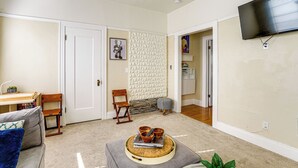 A living room with a sofa, a coffee table with a tray, a TV mounted on the wall, and a door leading to another room. - Pet-friendly Condo < 2 Mi to Alameda Beach! (Alameda)