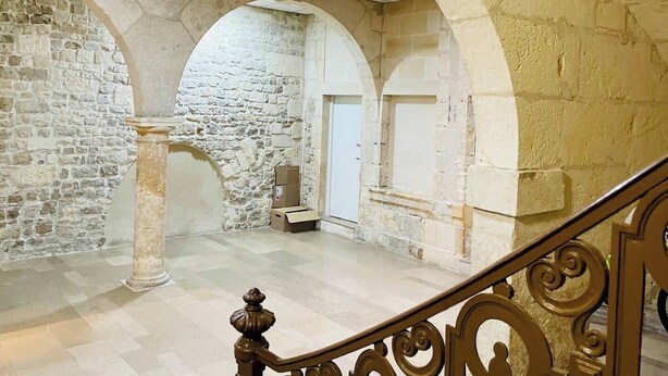 Un intérieur spacieux avec des murs en pierre, un sol carrelé et un escalier agrémenté de rampes décoratives.