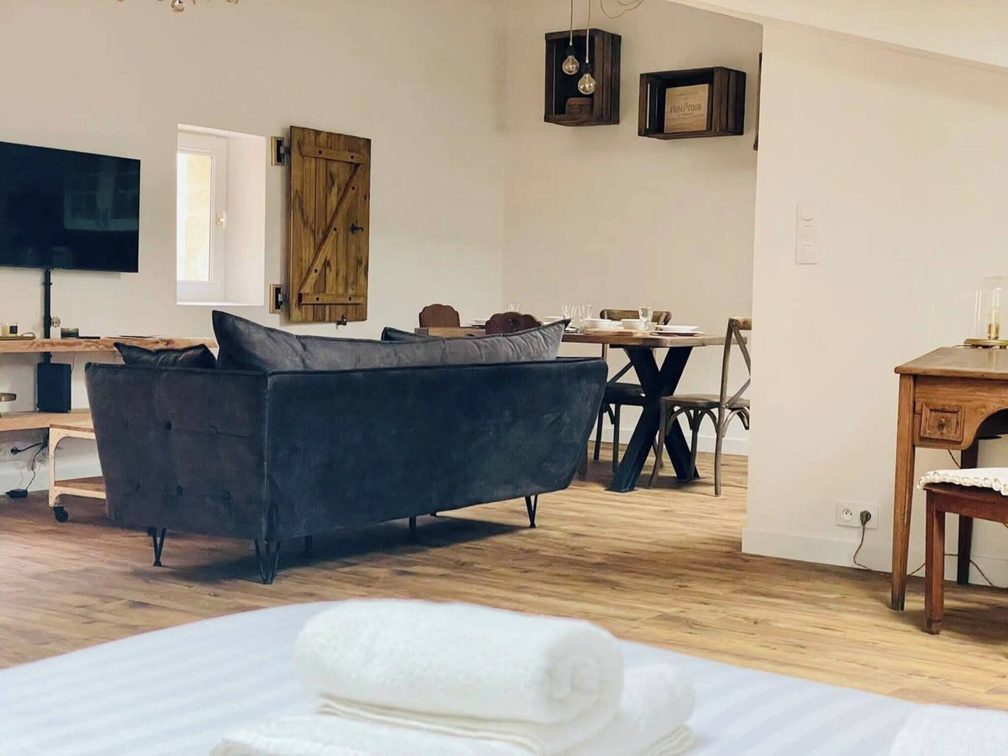 Un salon moderne avec un canapé foncé, une table à manger avec des chaises, une porte en bois et un téléviseur posé sur un meuble.