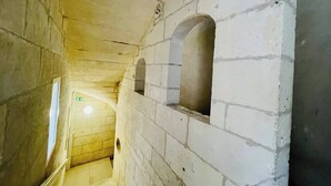 Un couloir étroit et faiblement éclairé, aux murs de pierre et aux ouvertures en arc de cercle.