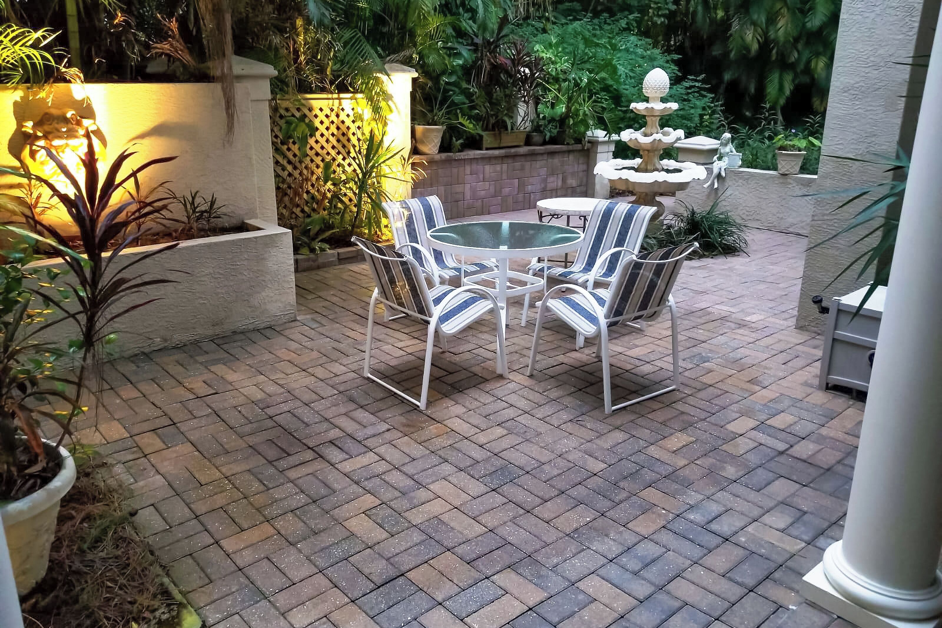 Een terras buiten met een betegelde vloer, witte metalen stoelen en een kleine tafel.