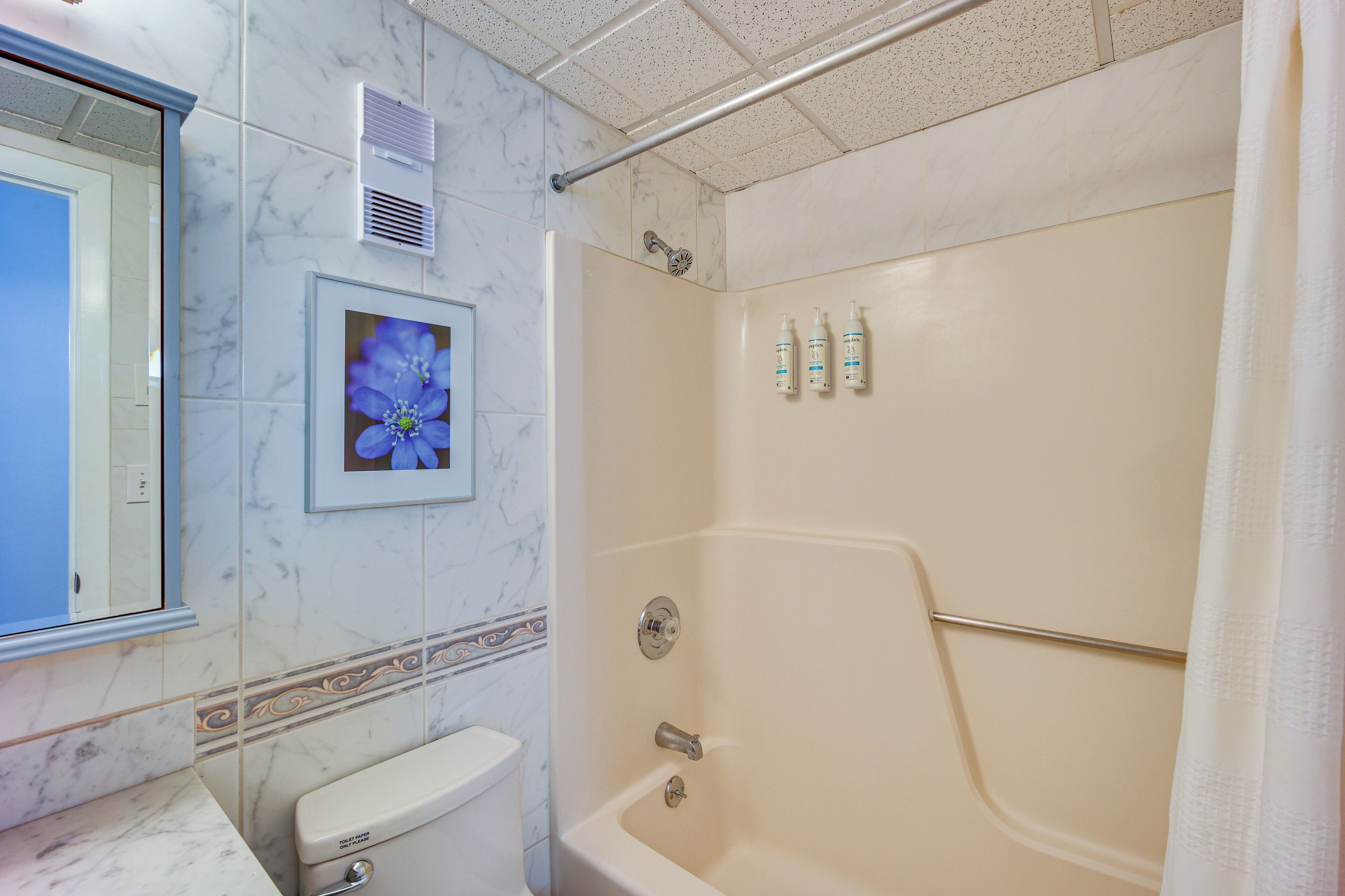 A bathroom with a toilet, a shower, and a framed picture of flowers on the wall.