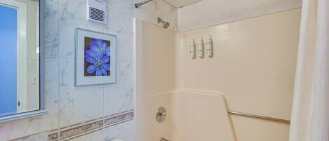 A bathroom with a toilet, a shower, and a framed picture of flowers on the wall.