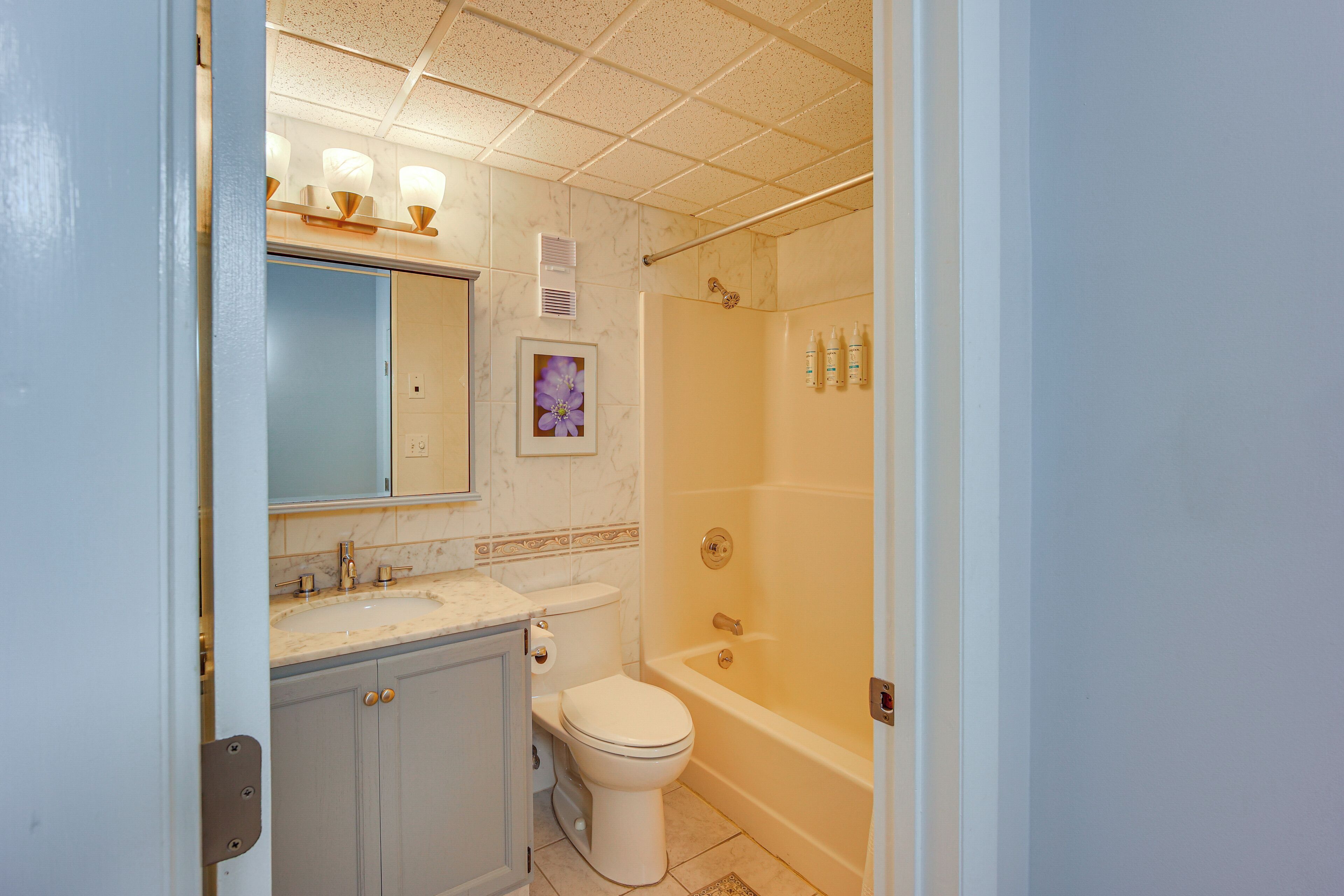 Een badkamer met toilet, wastafel, spiegel, douche en een lijst met een foto aan de muur.