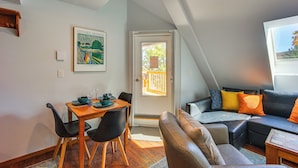 A cozy living room with a dining area, a sofa with cushions, and a door leading to an outdoor space. - Steps to Ski Lifts! Mountain Green Resort Retreat (Killington)