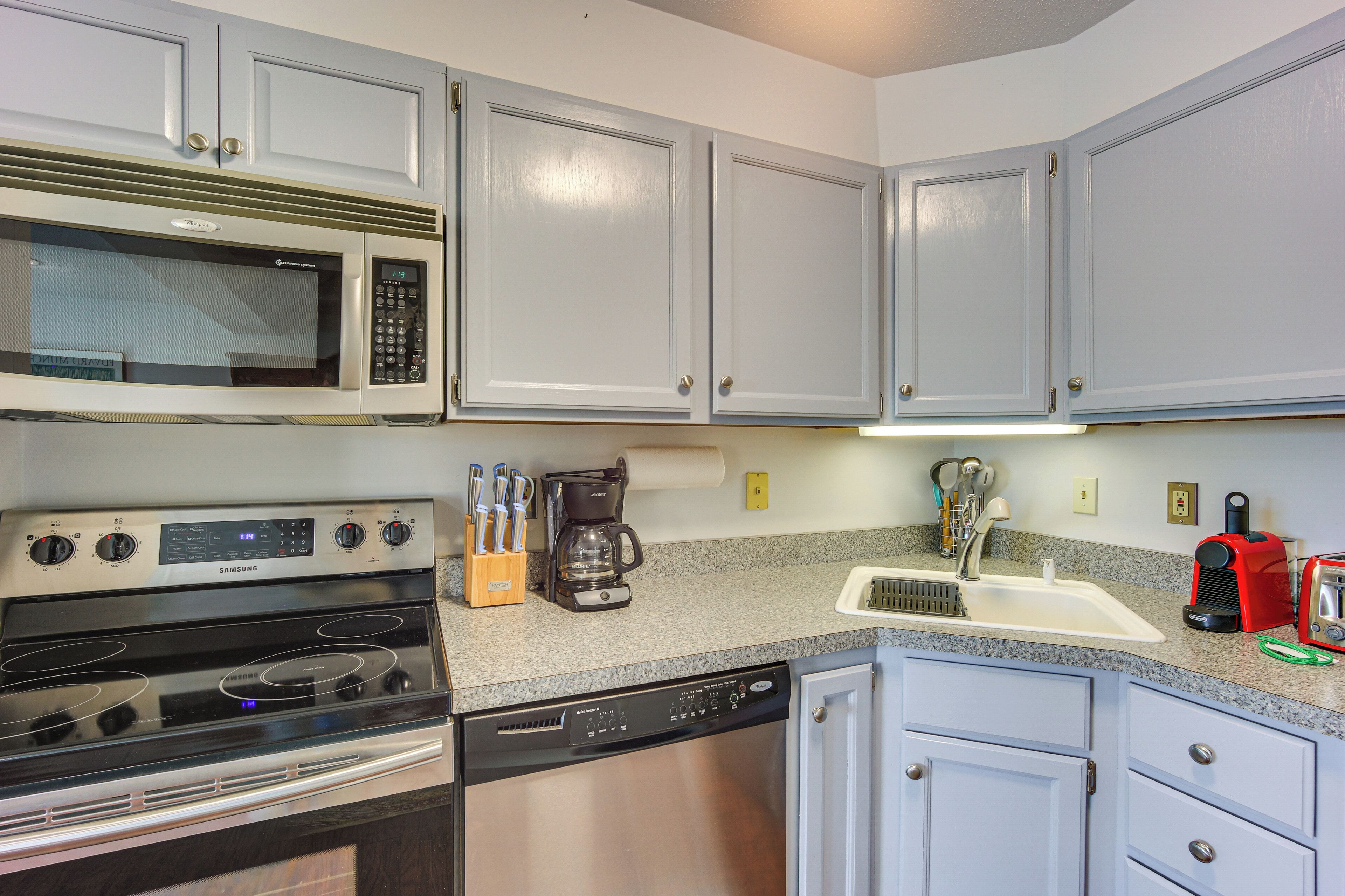 A kitchen with a microwave, stove, dishwasher, coffee maker, and a sink.