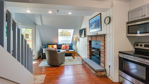 A modern kitchen with a built-in oven and microwave, a dining area with a table and chairs, and a cozy living room with a fireplace. - Steps to Ski Lifts! Mountain Green Resort Retreat (Killington)