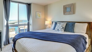 Ein Hotelzimmer mit einem großen Bett, Blick auf den Strand und einem Vorhangfenster.