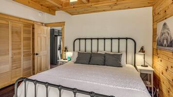 A bedroom with a large bed, wooden ceiling, and a wooden wall with a bear picture.