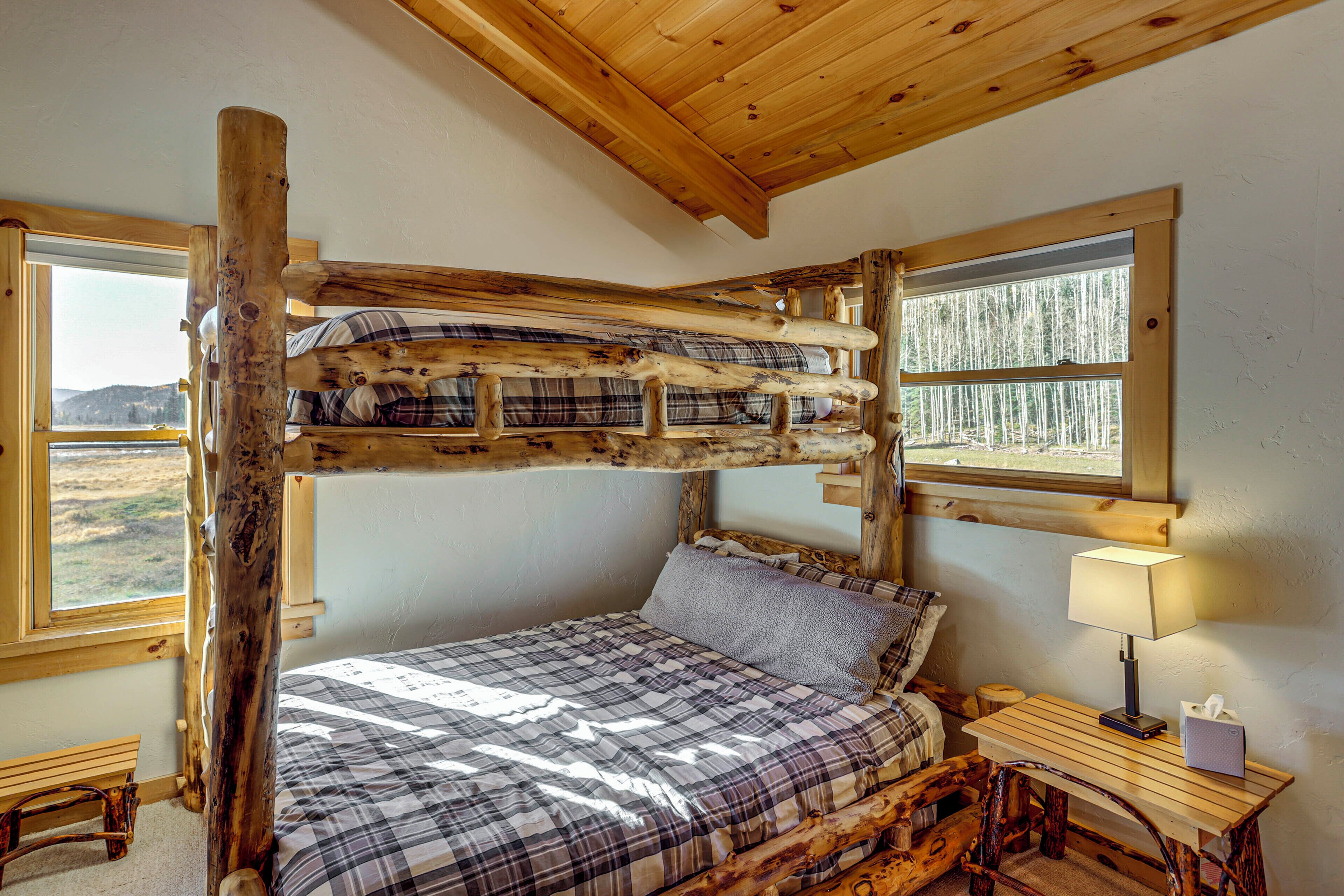 Un lit superposé avec une couverture à carreaux, un bureau en bois avec une lampe et une fenêtre donnant sur les arbres.
