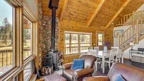 A log cabin interior with a stone fireplace, leather furniture, and large windows overlooking a forest. - Stunning San Juan Mtn Views: Cabin Near Skiing! (Durango)