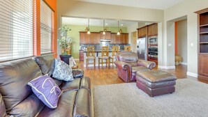 A modern living room with a leather sofa, ottoman, and a dining area with wooden chairs and a kitchen in the background. - Outdoor Oasis w/ Fire Pit: Pet-friendly Fresno Gem (Fresno)
