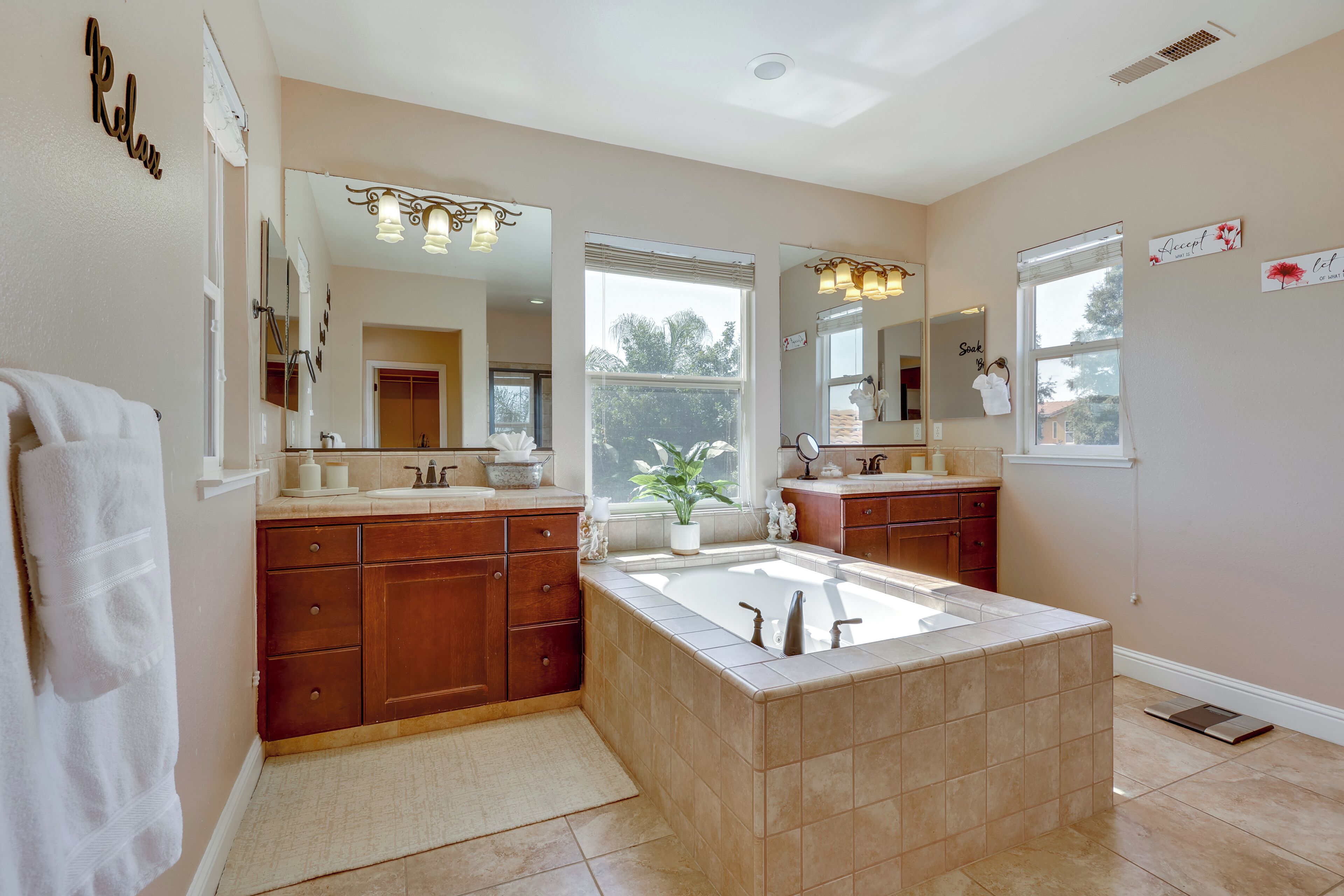 A modern bathroom with a large central sink, two vanity mirrors, and a window providing natural light.