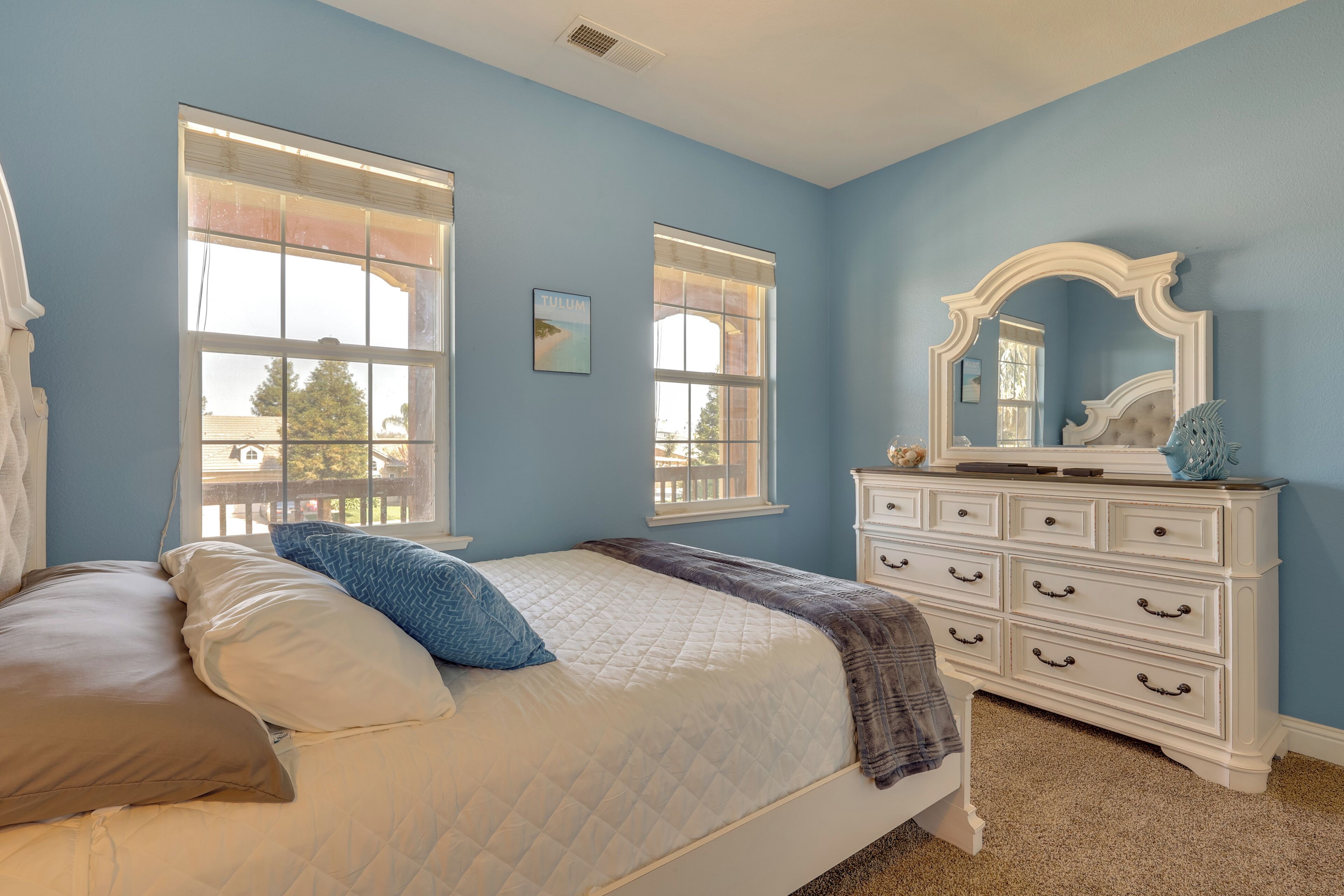 A bedroom with a bed, dresser, and two windows.