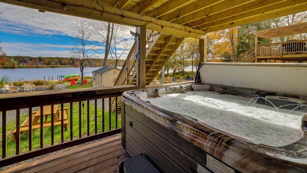 Eine Holzterrasse mit Whirlpool, Sitzgelegenheiten und Seeblick.