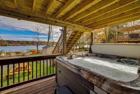 A wooden deck with a hot tub, outdoor seating, and a view of a lake. - Lakefront Pocono Retreat w/ Hot Tub & Movie Hub (Pocono Summit)