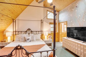 A four-poster bed with a wooden headboard, bedside tables with lamps, a large flat-screen TV, and a wooden cabinet. - 3 Mi to Snow Summit: Charming Home w/ Fenced Yard (Big Bear Lake)