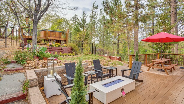 A wooden deck with outdoor furniture, a fire pit, and a red umbrella. - 3 Mi to Snow Summit: Charming Home w/ Fenced Yard (Big Bear Lake)