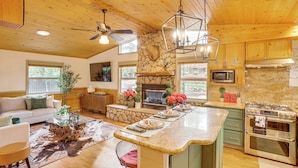 A spacious kitchen with a stone fireplace, wooden ceiling, and modern appliances. - 3 Mi to Snow Summit: Charming Home w/ Fenced Yard (Big Bear Lake)
