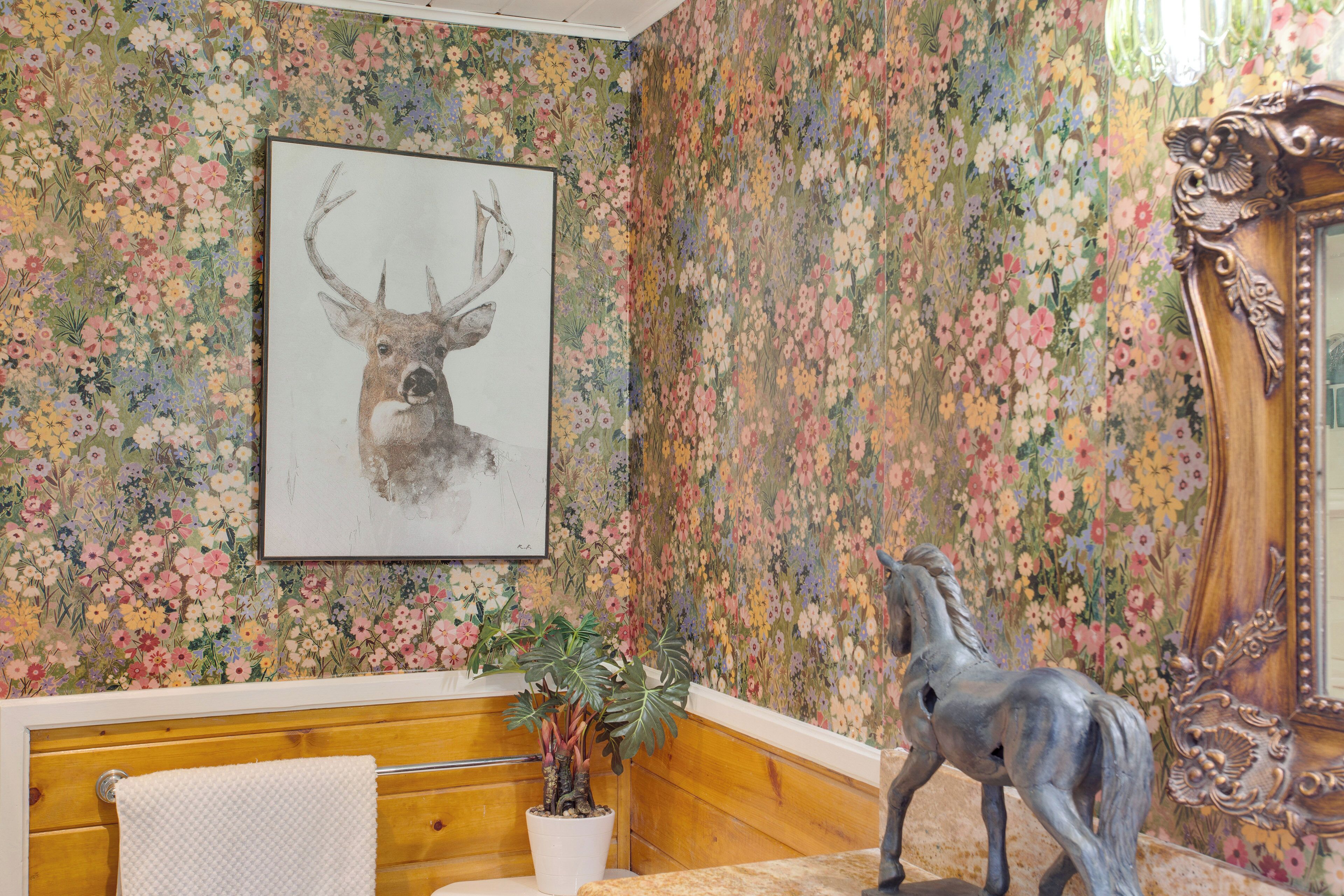 Een kamer met bloemenbehang, een hertenbeeld in een lijst, een houten hoofdbord, een potplant en een decoratieve spiegel.