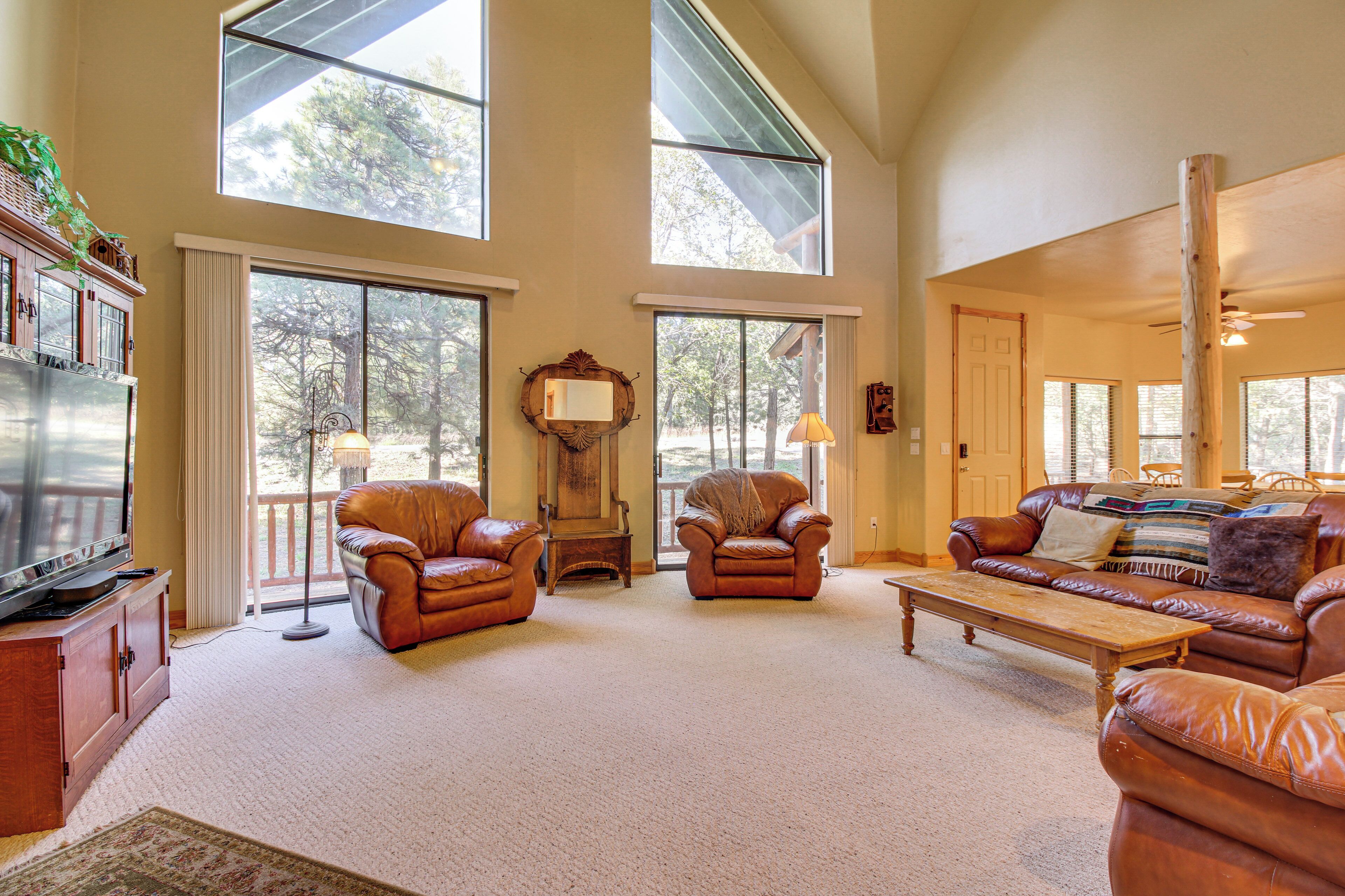 A spacious living room with leather sofas, a wooden coffee table, and large windows offering views of trees.