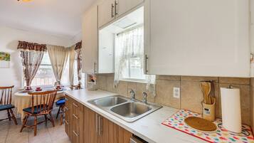 A kitchen with a double sink, wooden cabinets, a dining table with chairs, and a window with curtains.