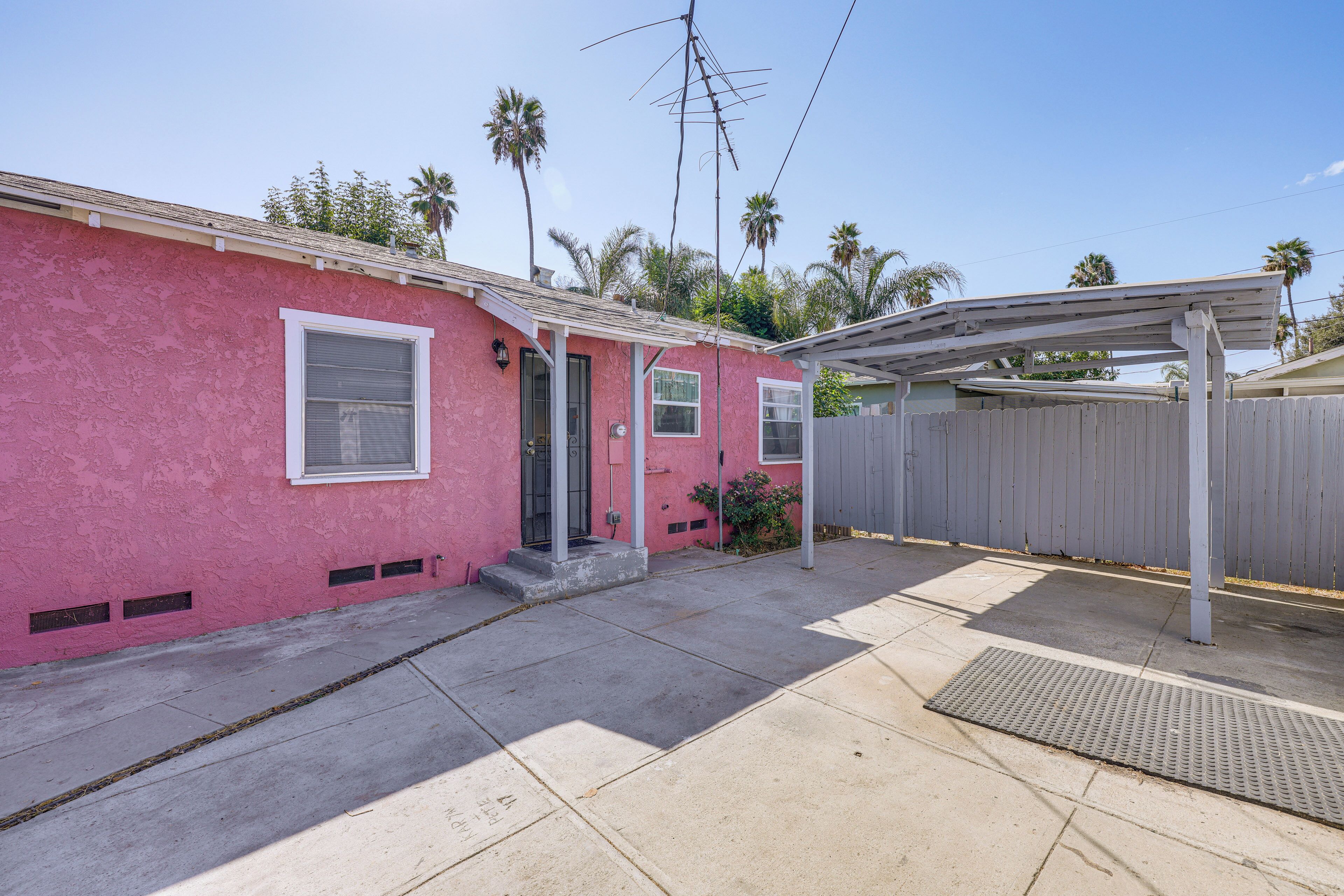 A pink house with a covered patio, a wooden fence, and a metal antenna.