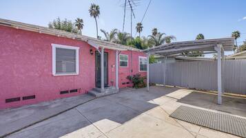 A pink house with a covered patio, a wooden fence, and a metal antenna.