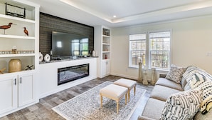 A modern living room with a fireplace, white cabinetry, a large flat-screen TV, and a cozy seating area with patterned cushions. - 8 Mi to Jiminy Peak Resort: Mtn-view Home w/ Deck (Stephentown)