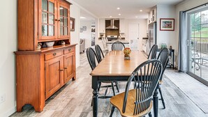 A dining area with a wooden table and chairs, a large wooden cabinet, and a kitchen in the background. - 8 Mi to Jiminy Peak Resort: Mtn-view Home w/ Deck (Stephentown)
